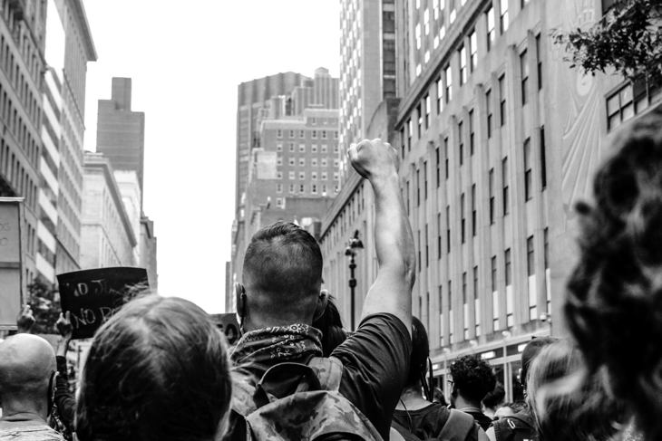 Ασπρόμαυρη φωτοτογραφία που δείχνει ανθρώπους να κάνουν πορεία σε σε έναν αστικό δρόμο.